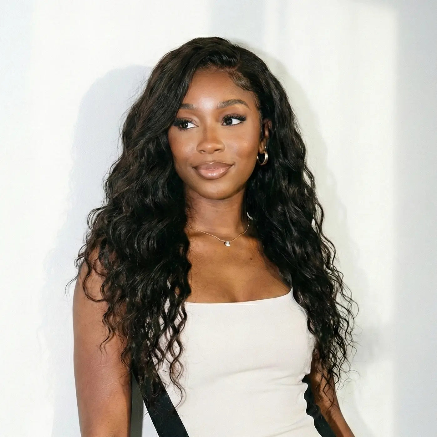 Woman with long, wavy hair wearing a white dress against a white background